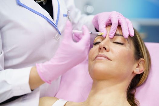 Aesthetic doctor injecting botulinum toxin into the forehead of her middle-aged patient. Facial treatment done in a cosmetic surgery clinic.