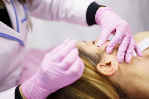 Doctor injecting PDO suture treatment threads into the face of a middle-aged woman.