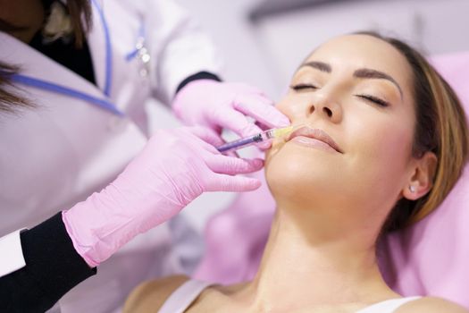 Doctor injecting hyaluronic acid into the mustache area of a middle-aged woman as a facial rejuvenation treatment.