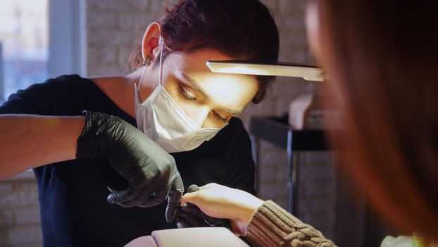 Working manicurist - nail master in medical mask doing professional manicure, telephoto