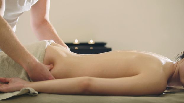 Young woman having classical massage in beauty spa, sesame oil, telephoto