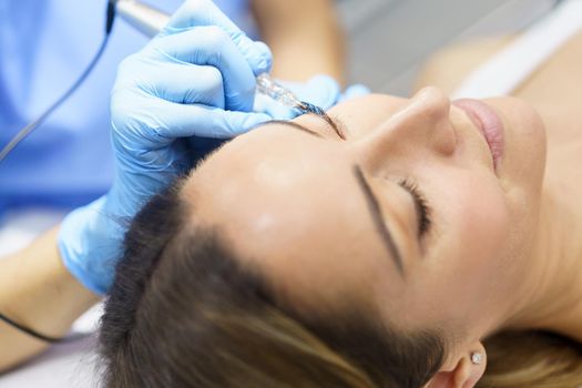 Permanent make-up for eyelashes of beautiful woman in a beauty salon. Close-up of beautician doing tattooing eyelashes. Micropigmentation treatment.