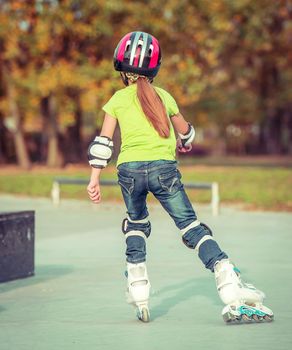Back view of little girl in helmet on roller-skates in park