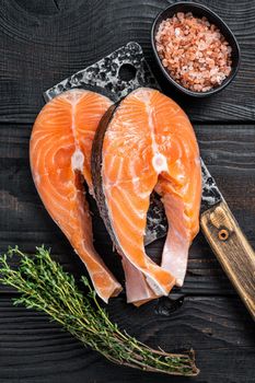 Fresh Raw Salmon steaks on butcher cleaver. Black wooden background. Top view.