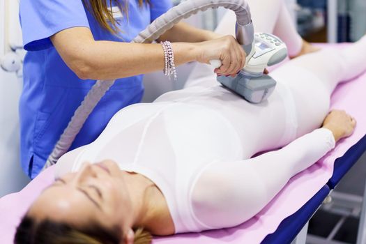 Middle-aged woman in special white suit having a anti cellulite belly massage with spa apparatus