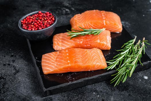 Raw salmon fillet steaks on marble board with herbs. Black background. Top view.