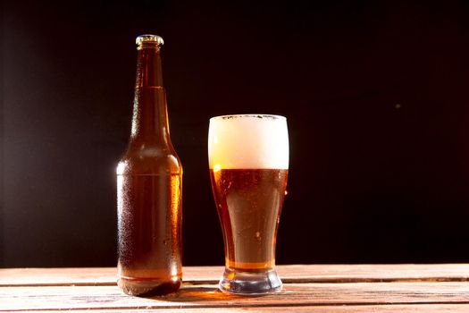 Bottle and glass of beer on a wooden table against a black background and copy space