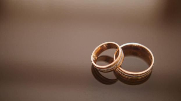 Golden wedding rings on mirror glasses table - one lies on top of another close up