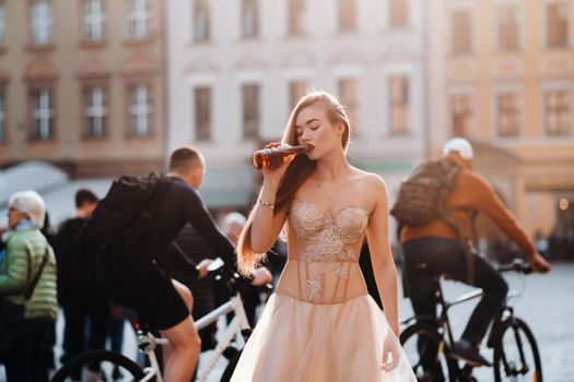 A bride in a wedding dress with long hair and a drink bottle in the Old town of Wroclaw. Wedding photo shoot in the center of an old Polish city.Wroclaw, Poland.