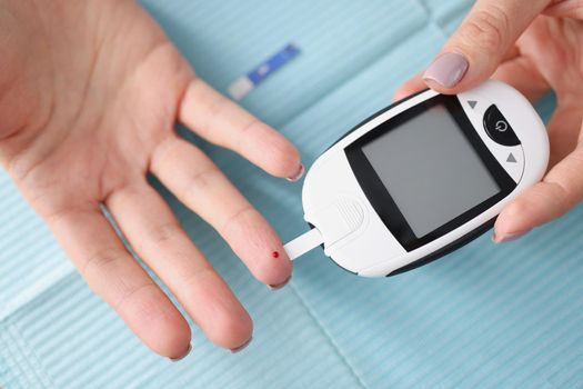 Close-up of female hands holding glucometer with strips. Medical portable device for determining approximate concentration of glucose in blood. Diabetic using glucose meter