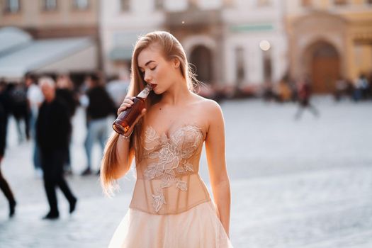 A bride in a wedding dress with long hair and a drink bottle in the Old town of Wroclaw. Wedding photo shoot in the center of an old Polish city.Wroclaw, Poland.