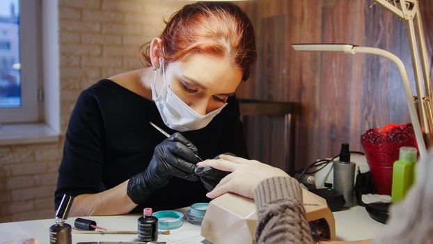 Labour of manicurist - nail master in medical mask doing professional manicure, telephoto