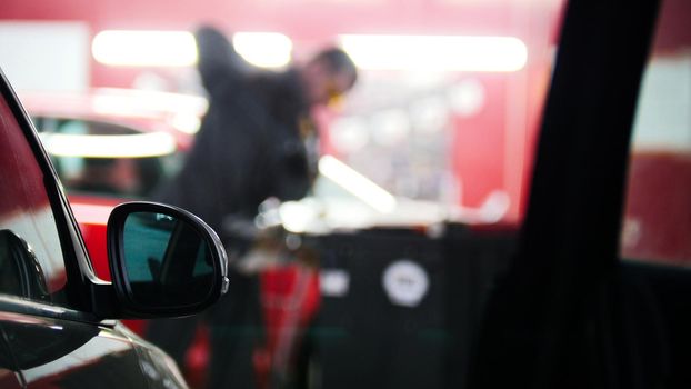 Defocused background - car service - man worker repairing automobile, telephoto