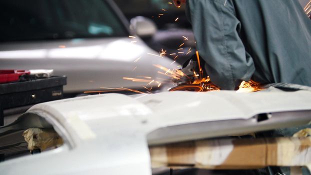 Professional car service - worker grinding metal with a circular saw, rear view, telephoto