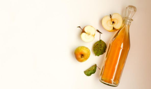 A bottle of apple cider vinegar and apple fruit composition with leaves on white background. copyspace.