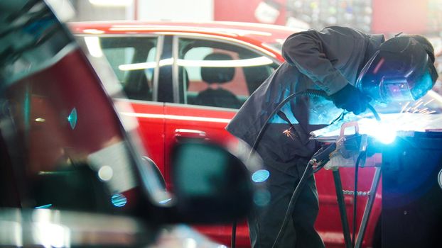 Industrial concept: worker in helmet repair detail in car auto service, telephoto