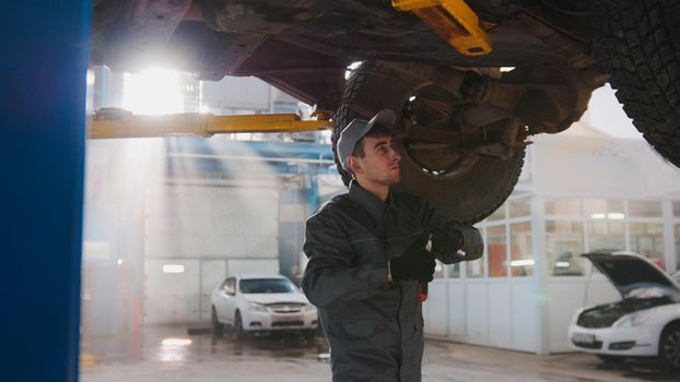 Garage automobile service - a mechanic under bottom of car checks the wheel, close up, horizontal