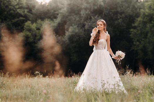 On the wedding day, an Elegant bride in a white long dress and gloves with a bouquet in her hands stands in a clearing enjoying nature. Belarus