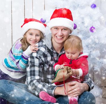 Christmas photo of an attractive man and his cute daughters in Santa Claus hats around a decorated Christmas tree