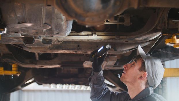 Mechanic is checking the bottom of car in garage automobile service, close up, telephoto