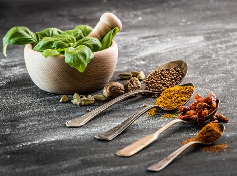 fresh basil in a wooden mortar and spices spoons