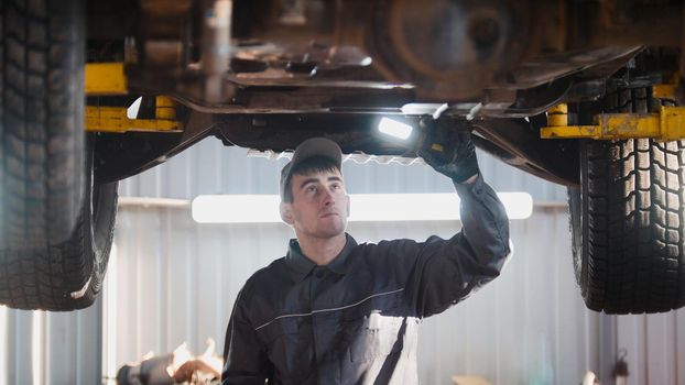 Mechanic with thr lamp is checking the bottom of car in garage automobile service, wide angle, telephoto