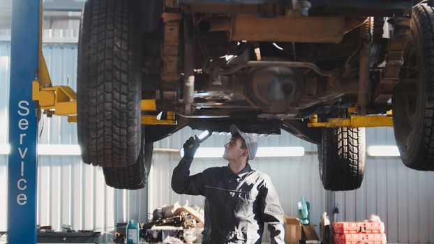 Mechanic with thr lamp is checking the bottom of SUV car in garage automobile service, wide angle, telephoto