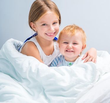 Two pretty little sisters in white T-shirts in bed