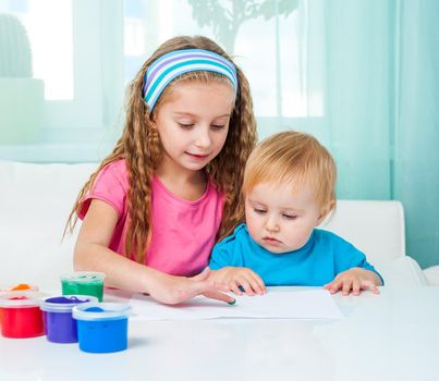 two cute sisters draw finger paints at home in bright living room