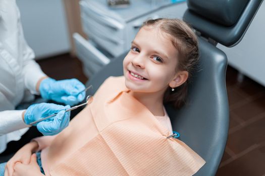 Cute smiling young caucasian girl visiting dentist, having his teeth checked by female pediatric dentist in dental office.