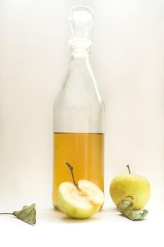 a half-filled bottle of apple cider vinegar, whole and half an apple with leaves on white background.