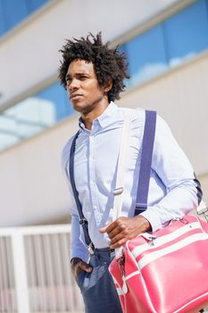 Black businessman with afro hair walking near an office building with a sports bag.