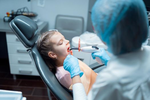 Back view of Female dentist who providing tooth restoration and filling with curing polymerization UV lamp for little girl patient