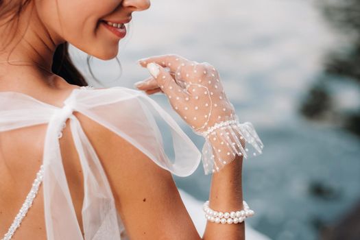 An elegant bride in a white dress and gloves is sitting by the lake in the Park, enjoying nature.A model in a wedding dress and gloves in a nature Park.Belarus