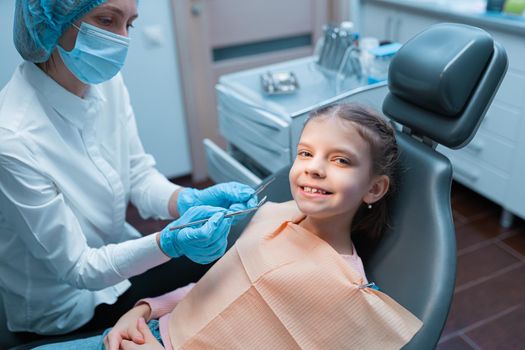 Cute smiling young caucasian girl visiting dentist, having his teeth checked by female dentist in dental office.