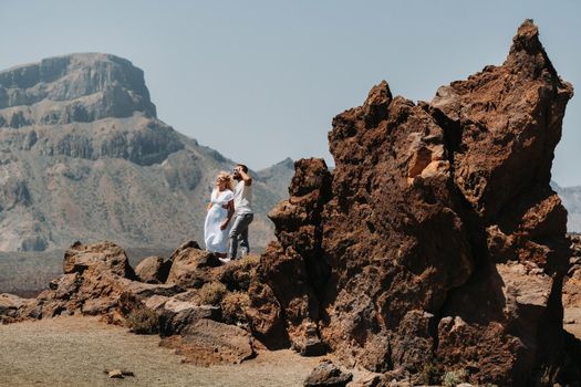 a guy and a girl in white clothes and glasses stand in the crater of the El Teide volcano, a Couple stands on a mountain in the crater of a volcano on the island of Tenerife, Spain.