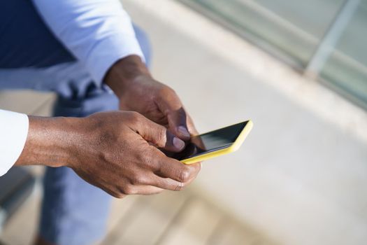 Hands of unrecognizable black man using a smartphone sitting on a urban step.