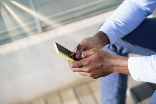 Hands of unrecognizable black man using a smartphone sitting on a urban step.