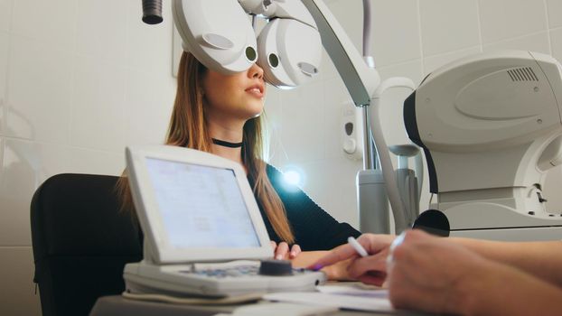 Blonde young female doing eye test with optometrist in medical center, close up