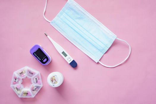 Surgical masks, thermometer and pills on pink background .