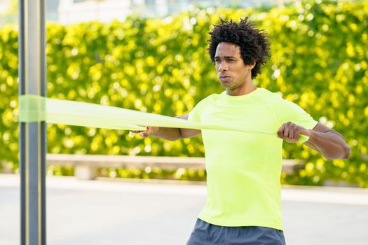 Black man working out with elastic band outdoors. Young male exercising in urban background.