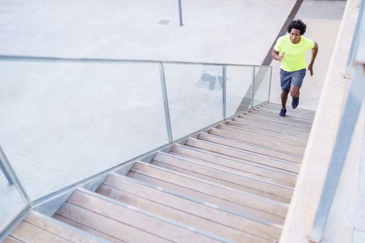 Black man running upstairs outdoors. Young male exercising in urban background.