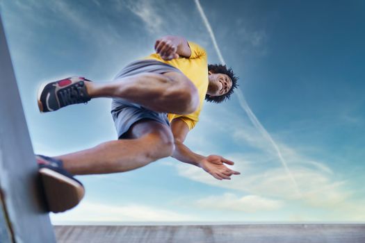 View from below of black man jumping on his run. Young male exercising in urban background.