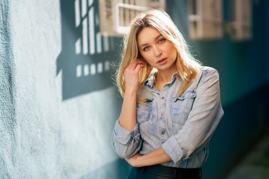 Blonde woman wearing denim shirt and black leather skirt standing in the street. Pretty russian female.