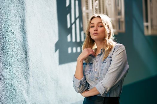 Blonde woman wearing denim shirt and black leather skirt standing in the street. Pretty russian female.