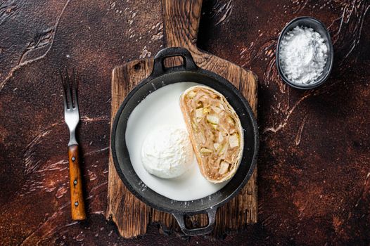 Apfelstrudel strudel with cinnamon, powdered sugar and vanilla ice cream in a pan. Dark background. Top view.