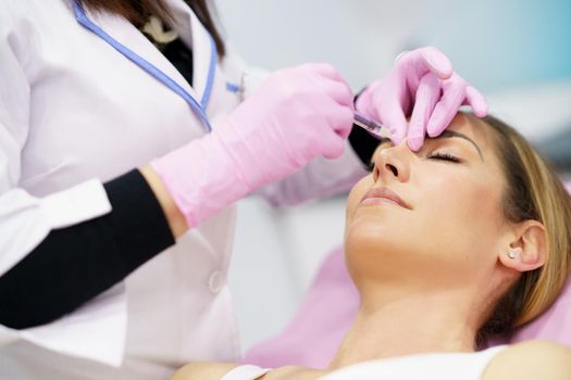 Doctor performing rhinoplasty by injection of hyaluronic acid in the nose of his patient, a middle-aged woman.