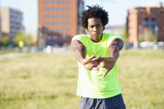 Black man doing arms stretches after running outdoors. Young man exercising in urban background.