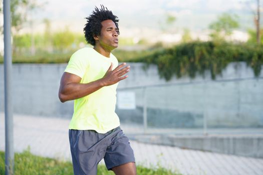 Black athletic man, afro hairstyle, running in an urban park. Young male exercising in urban background.