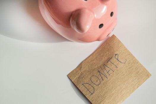 Cute pink piggy bank on a white background and a mock-up of wrapping paper with the inscription DONATE.